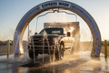 Muddy work truck entering express wash arch with strong underbody rinse jets