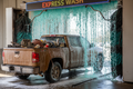 Dirty contractor pickup covered in dust entering foam curtain of express wash